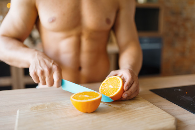man-with-naked-body-cuts-orange-on-the-kitchen-nude-male-person-preparing-breakfast-at-home-food-preparation-without-clothes_266732-5815